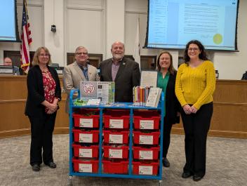 3 Library staff and 2 City leaders pose behind Community Comfort Cart at city council meeting. 