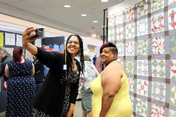 Palatine Public Library Workshop Manager Selicia Applegate and Palatine resident Tiffany Wilhoite stand in front of exhibit's Freedom Quilt. They are smiling as they take a selfie.
